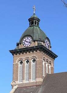 Steeple with copper dome, topped by cross; clock dials face in four directions