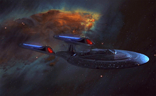 A spaceship glides out of a vibrant, multicolored nebula. The ship is composed of a saucer-shaped primary hull, connected to a thicker secondary hull. Paired glowing engines are attached to the secondary hull via swept-back struts.