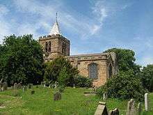 A church seen from a distance; on the left is a tower with a pyramidal spire and a round clock face; the body to the right is crenellated. In the foreground are gravestones and on each side are bushes and trees
