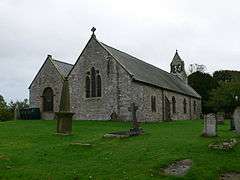 A simple church with a double nave, that on the right being the higher; at the far end is a bellcote containing two bells; in the foreground are gravestones in various shapes, including a cross