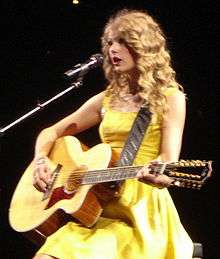 Taylor Swift performing with a guitar in a yellow dress