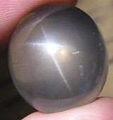 A bluish gray round cabochon of quartz showing a four rayed star effect under intense lighting.