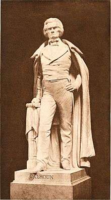 Life sized statue, standing with full cloak to ankles, left hand on hip, right hand on book, serious and distinguished demeanor.