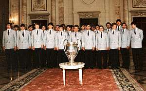group of about 20 identically dressed men standing shoulder-to-shoulder with a trophy in front of them