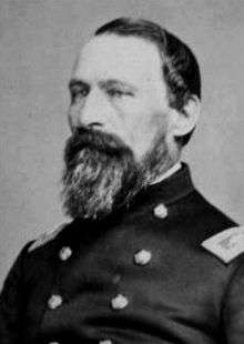 Head of a middle aged white man with a full beard and neatly combed hair, wearing a double-breasted military jacket.