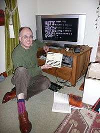 Steve Vickers sitting next to a flatscreen television which is connected to a Jupiter ACE.