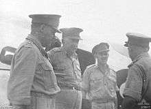 Four men in uniform with peaked caps talking to each other.
