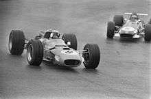Black-and-white photograph of two Formula One cars driving on a wet track