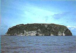 A rocky island with steep sides rises sharply out of the water.