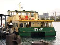 Rear of a ferry boat with jetty to its left. Boat has "Shortland" and "Newcastle" on the back