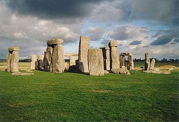 Standing stones at Stonehenge in the sunlight, with dark clouds above