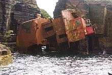 View of part of a wrecked ship, wedged on its side in a gap between cliff faces