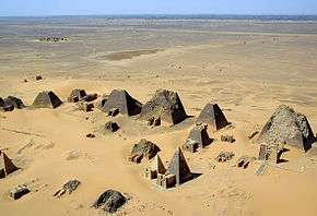 An aerial view of a dozen pyramids in relatively bad shape in the foreground, and a deserted view in the background.