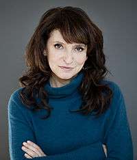 Photo of Susanne Bier standing in front of a grey wall in 2013.