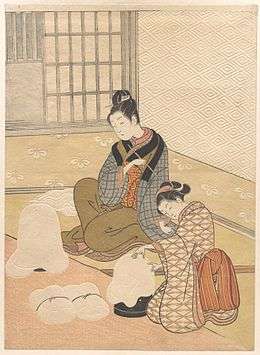 Colour print of two finely dressed Japanese women by a heater.  The wallpaper and other items are extensively embossed.