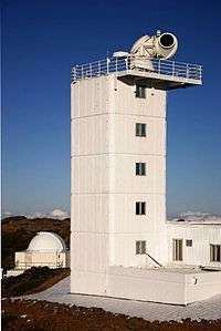 Photo of six-story building with fenced balcony containing large telescope