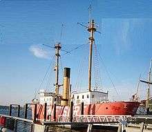 Photograph of Lightship No. 83, Relief, at dock in Seattle as a museum ship, its light masts rising to the sky and its red hull painted with its contemporary name Swiftsure.