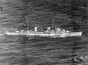 Black-and-white aerial photograph of a two-funnelled cruiser underway. Alternating light and dark bands are painted on the side of the ship.