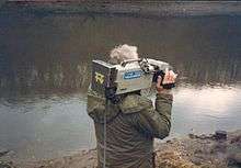 A reporter standing beside a river holding a camera with the Tyne Tees logo.