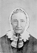 A black and white picture of an elderly woman wearing a white bonnet and dark clothing.