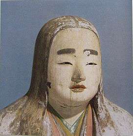 Head and shoulder portrait of a female statue with long hair, painted eyebrows, colored lips and cloths.