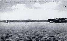 A black-and-white illustration showing the lighthouse at left surrounded by water and the shore at right. Faint writing across the top reads "Hudson River, showing Lighthouse and Maxwell–Briscoe factory, Tarrytown, N.Y."
