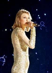 Taylor Swift is performing onstage with a mic in her right hand
