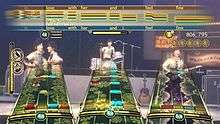 A video game screen shot that shows three "note tracks" along the bottom half and a horizontal bar like a musical staff for the vocalist, overlaid against other interface elements such as a scoring meter, star tracking, and performance meter, and images of the virtual Beatles avatars playing at the specific venue