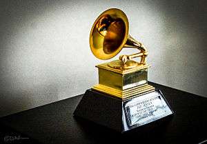 A gold trophy in the shape of a gramophone on top of a base with a plaque on it, set on top of a table