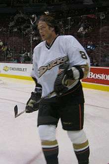 A brown haired hockey player in a white and black uniform with the wordmark "Ducks" across his chest skates as he looks into the distance.
