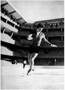 A woman does a spiral on skates in a stadium.