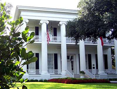 A white Greek-revival-style mansion with 6 tall columns visible at the front and two stories