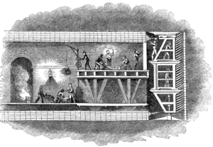 Illustration of a cross section through the Thames Tunnel showing miners on the platforms of a tunnelling shield digging at the face of the excavation whilst others behind on a wheeled platform construct the tunnel lining in brickwork