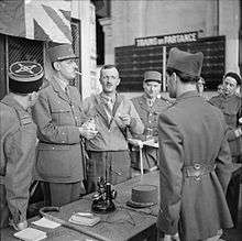 Six men in uniforms. De Gaulle is wearing his kepi and smoking a cigarette.