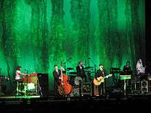 The Decemberists perform in formal attire on a green stage