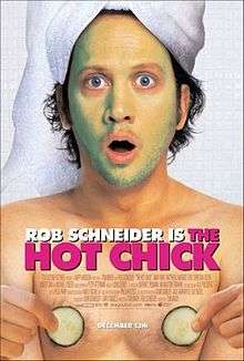 Rob Schneider with a towel covering his hair, and green facial cream covering his face, and holding two cucumber slices in his hands over his chest.
