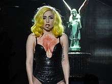Lady Gaga performing in a black dress, with red paint around her bosom