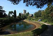 Pool of water in an area of trees and shrubs. In the background is the cathedral.