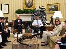 President Obama sits on the Iron Throne in the Oval Office of the White House, surrounded by other people