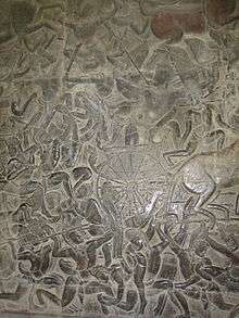 A black stone relief depicting a number of men wearing a crown and a dhoti, fighting with spears, swords and bows. A chariot with half the horse out of the frame – is seen in the middle.