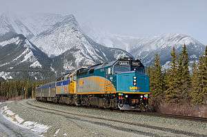 Passenger train rounding a bend, with snow-capped mountains in background