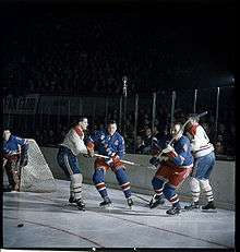 Five men playing hockey in a crowded arena.