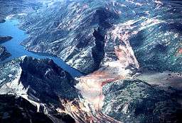 An aerial picture of a de-stabilized mountain sliding and creating a dam and lake. Various construction activity is present to the left of the slide area.