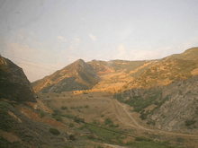 View through a dirty window, showing power lines in the foreground and a scarred mountain with the scar leading to an earthen dam.