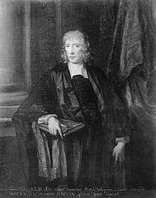 A man with light-coloured, slightly curly, hair. He is wearing black clothes and a black gown, and holds a large book in his right hand