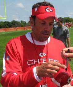 Haley wearing a red Kansas City Chiefs sweatshirt and red Chiefs visor while autographing a Chiefs baseball cap