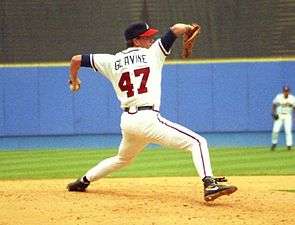A left-handed baseball pitcher wearing a black baseball cap, white uniform, and black shoes; the back of his uniform has the lettering "GLAVINE" and the number 47, in a throwing stance.
