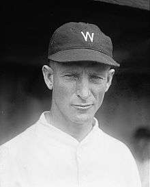 A wearing a white baseball jersey with a dark cap with a white "W" on the center.