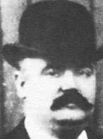 Black and white photograph of a man wearing a bowler hat. He also has a thick black moustache