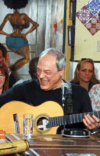 A man in a black shirt is playing a guitar next to a table